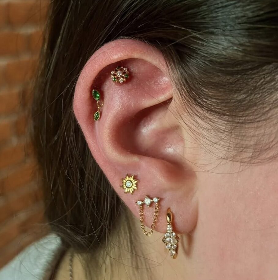 Oreille avec plusieurs piercings en titane doré : hélix, conch, lobe avec chaînette
